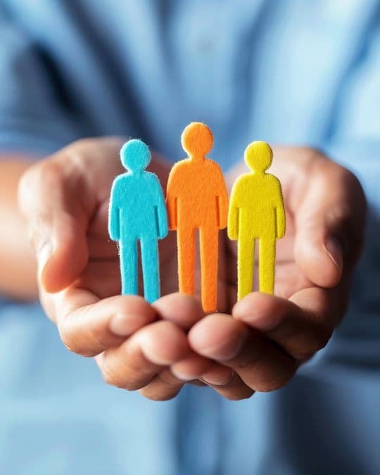 Imagen de manos que sostienen figuras humanas de colores, simbolizando inclusión, diversidad y apoyo emocional.